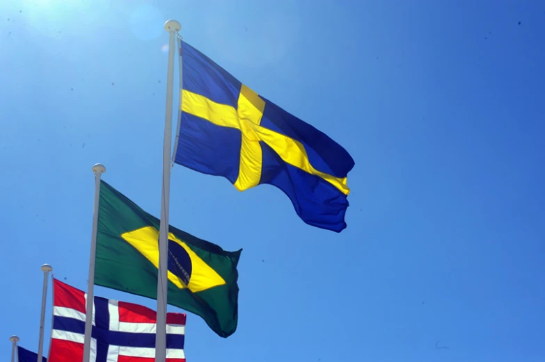 three flags blowing in the wind against a blue sky