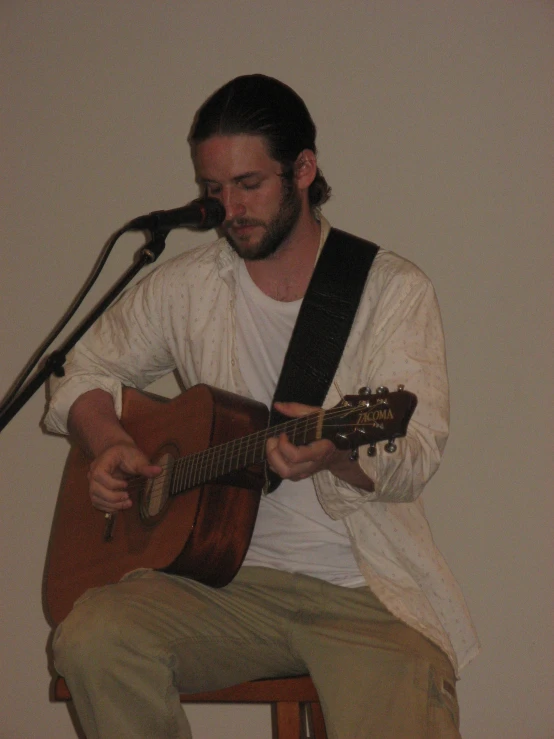a man playing an acoustic guitar while sitting on a stool