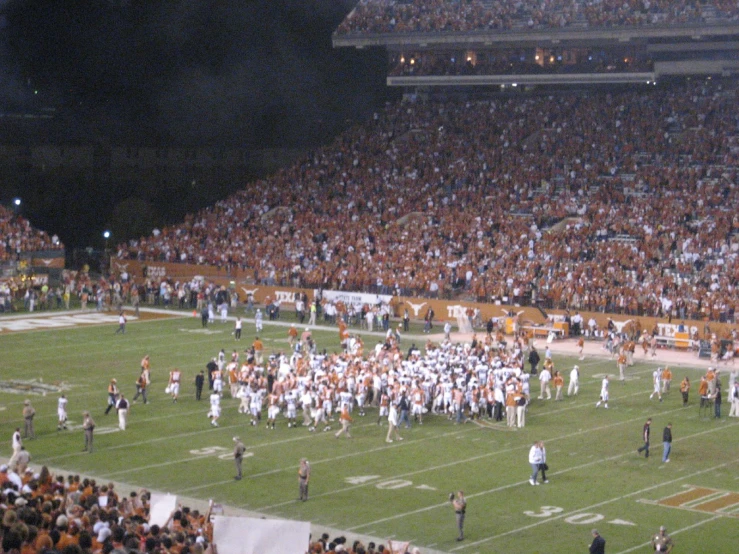 many people stand on a football field as two teams huddle