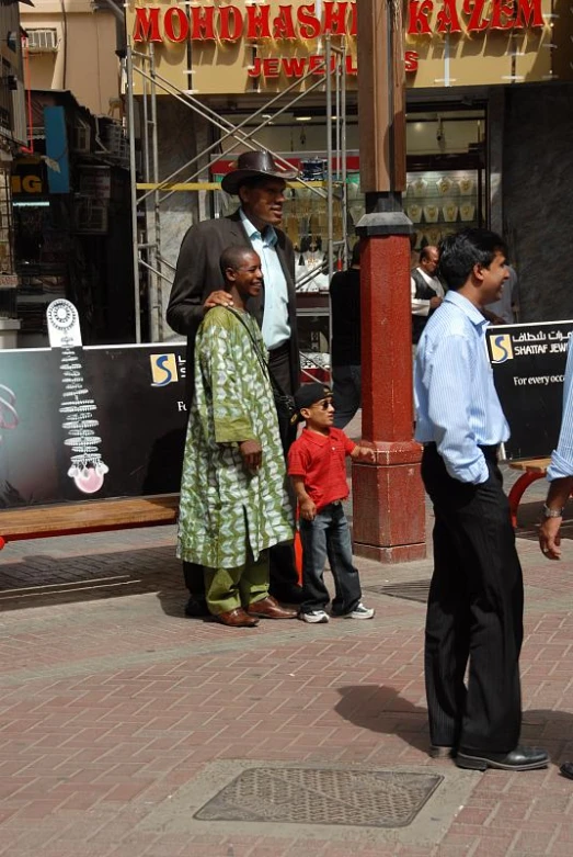 a woman in a long dress standing next to two men in front of shops