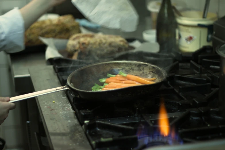 a person frying carrots in a frying pan