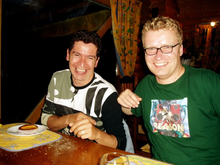 two men sitting at a table and one in a green shirt