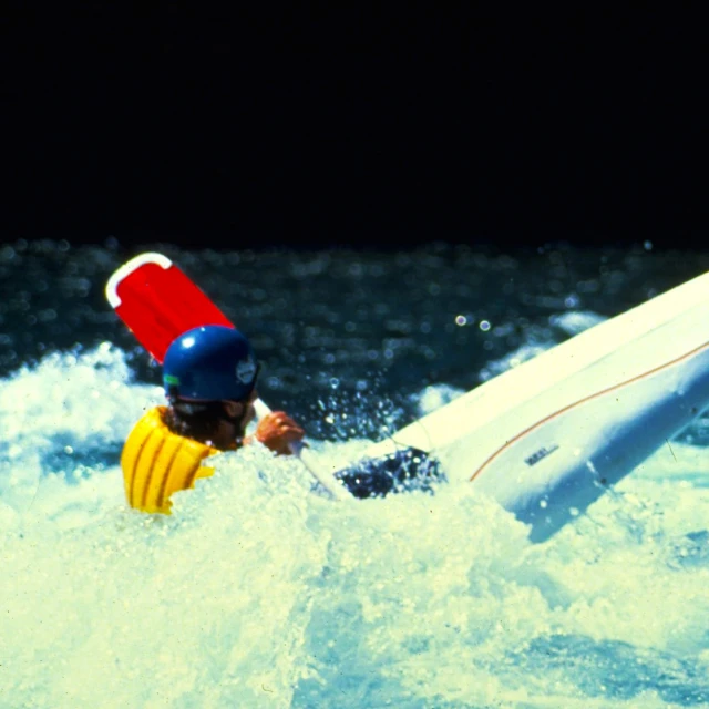 a man in yellow jacket with hat on holding surfboard in water