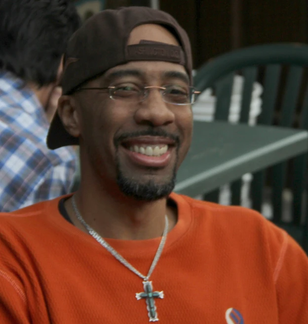 a smiling man wearing a red shirt with a cross on it