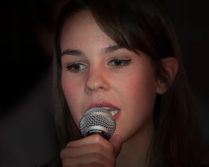 a woman standing in front of a microphone, making a gesture