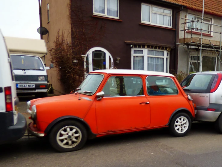 an orange small car parked next to a red van