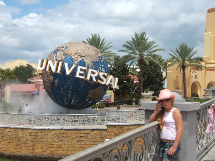 a young woman poses with her arm on the back of a handrail near a sign that reads universal with steam coming from behind it