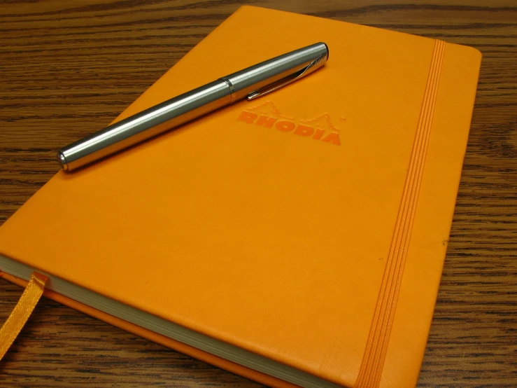 an orange spiral notebook and a stylus on a table