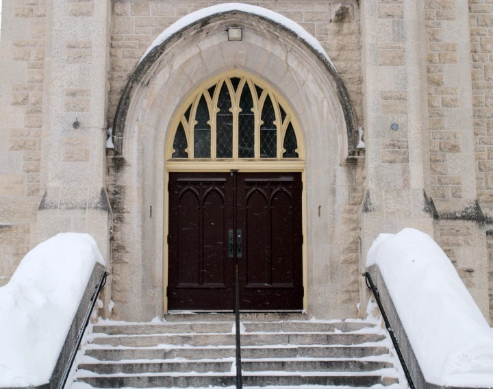 two black doors with white stairs and a building that has snow on the bottom