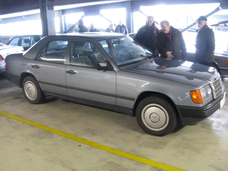 a group of people are gathered around an old mercedes