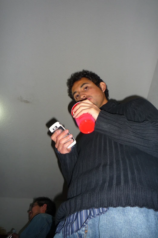 a man drinking from a red cup and holding a cell phone