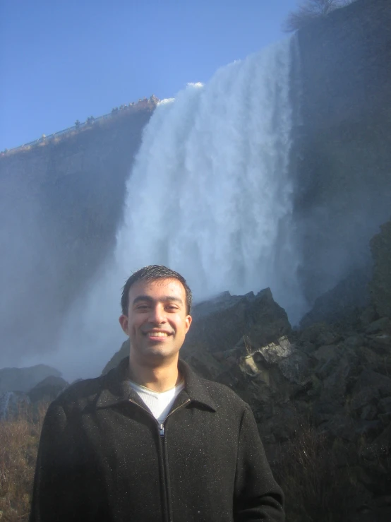 man standing in front of geyser at the base of a tall waterfall