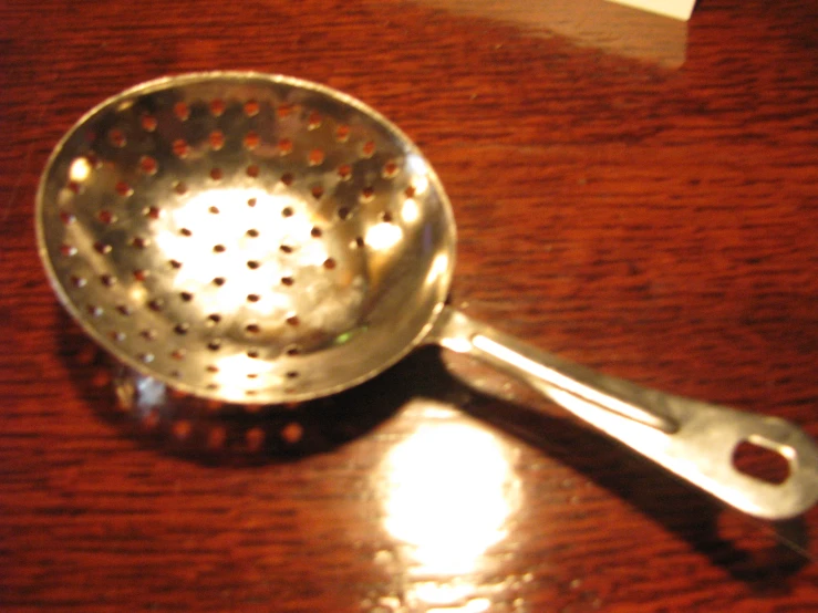 the metal strainer is on the wooden table