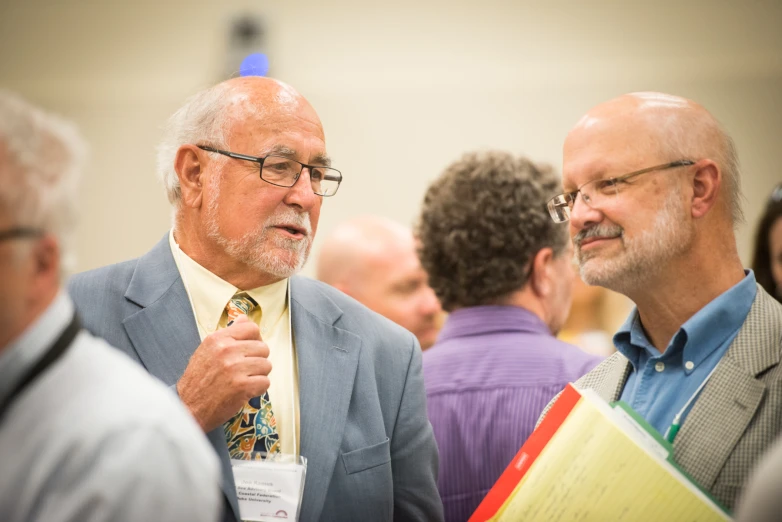 two older men speak with each other in a crowded room