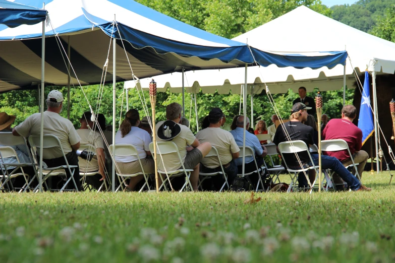 people are gathered under tent chairs near a row of trees