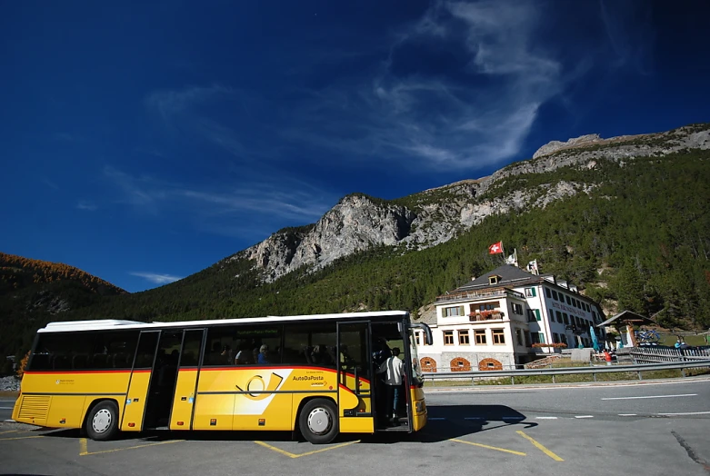 a yellow passenger bus parked next to a mountain