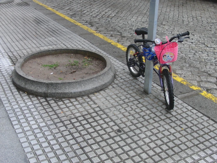 a bike is tied up to the pole on the sidewalk