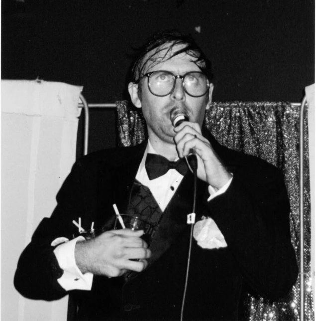 a man wearing glasses holds his mouth open to sing