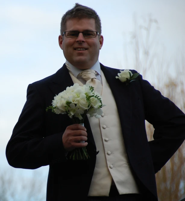 a man wearing glasses and a suit holding flowers