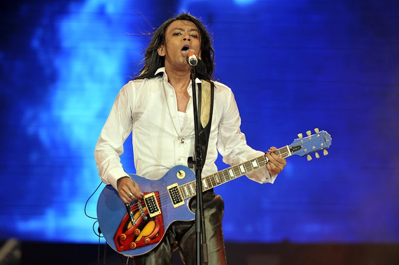 a man in white shirt and black pants holding a blue guitar
