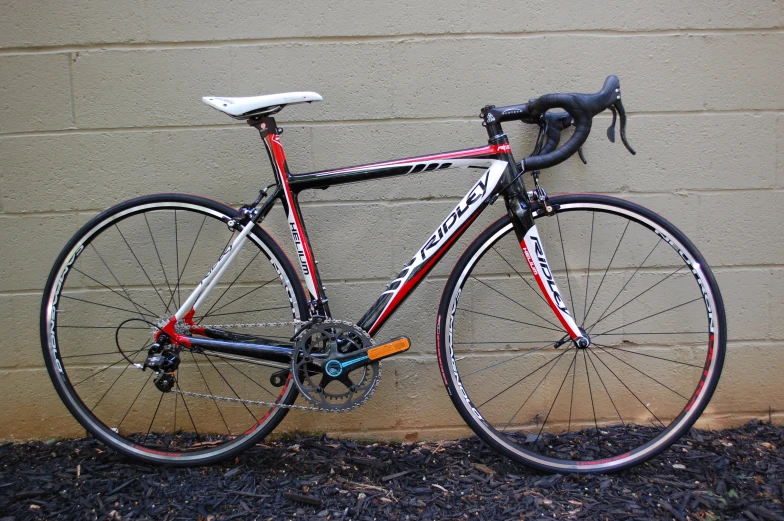 a red, white and black bike leaning against a brick wall