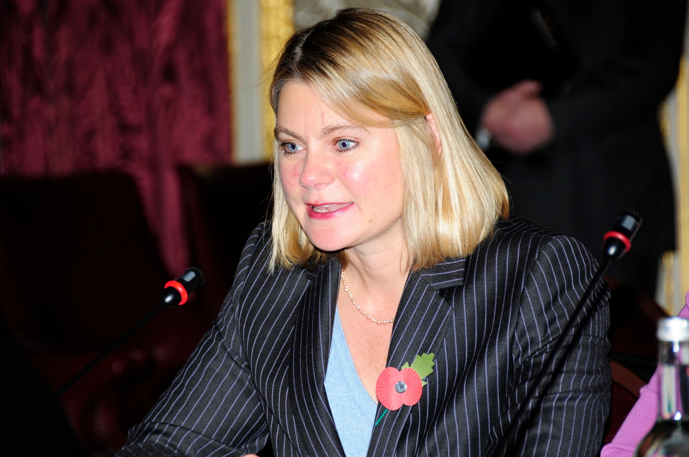 blonde haired woman wearing pinstripe jacket and necklace sitting down