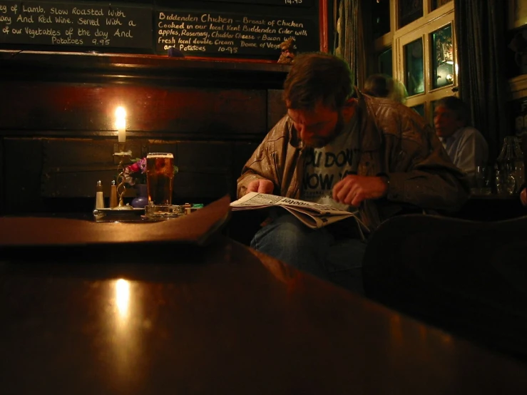 the man is looking at the newspaper while sitting in the bar