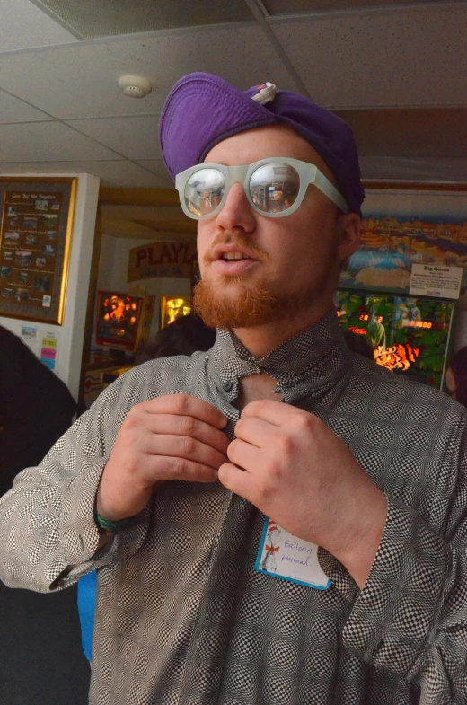 a man wearing sunglasses and a purple hat putting on his tie