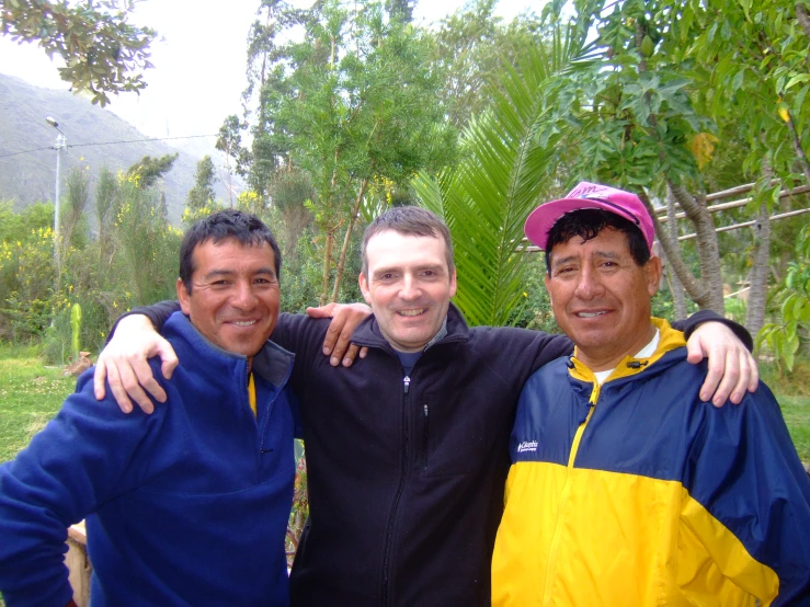 three men, one standing up, wearing rain jackets