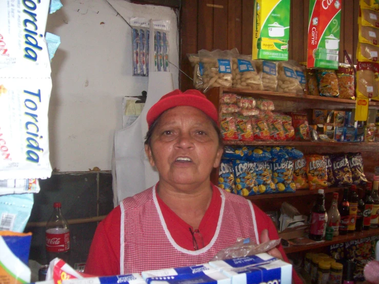 an elderly woman sitting in front of shelves with snacks