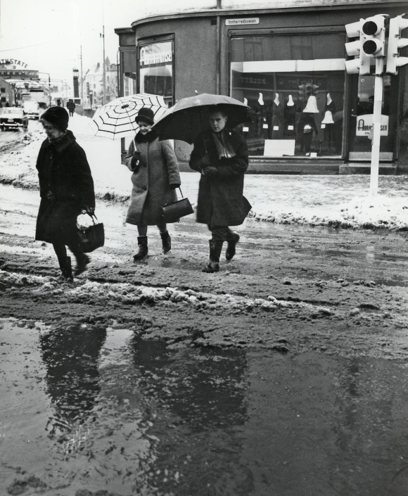 three women crossing the street with umbrellas in a black and white po