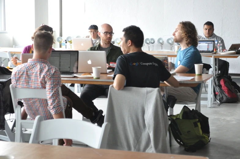 group of people sitting in chairs at tables with laptops