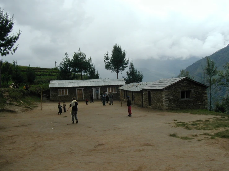 several people in a village in front of a building with mountains and clouds
