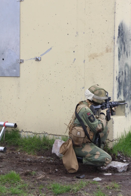 a soldier kneeling in front of a building with a rifle