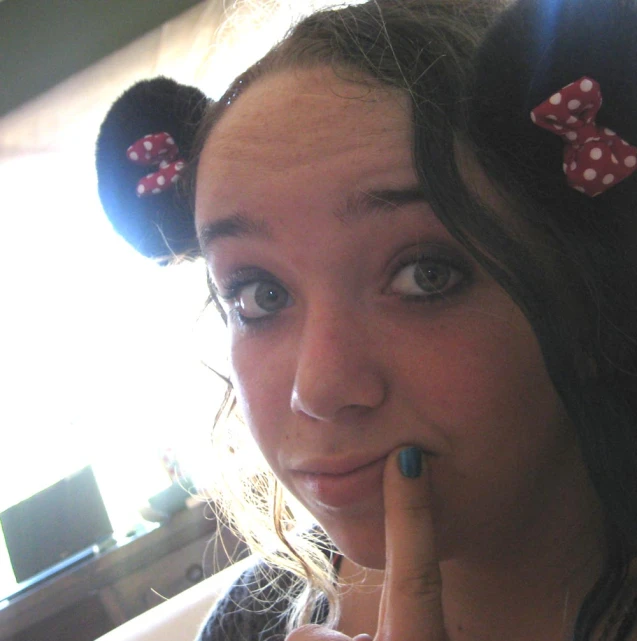 a lady wearing a blue and red minnie mouse headband with a finger on her lips