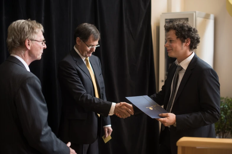 two men shaking hands, one wearing a suit and the other in a tie