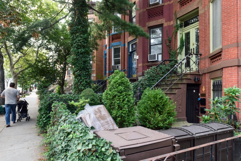 a couple of people walking down a sidewalk past large brick buildings