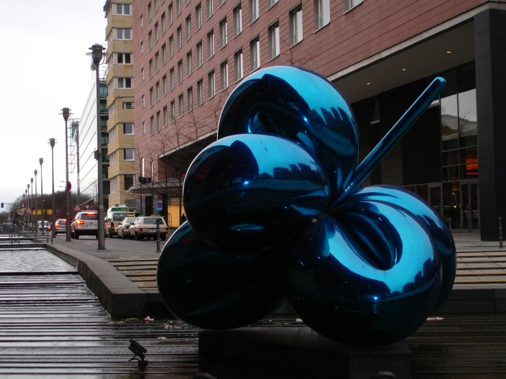 the blue sculpture stands on the city sidewalk