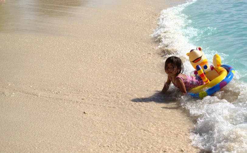 a girl in a swim suit on the beach with a bear float