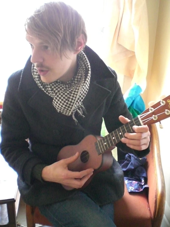 boy in black jacket sitting holding guitar in hand