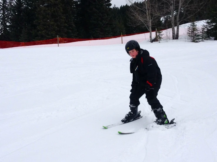 a child wearing snow shoes and black gear, is snowboarding