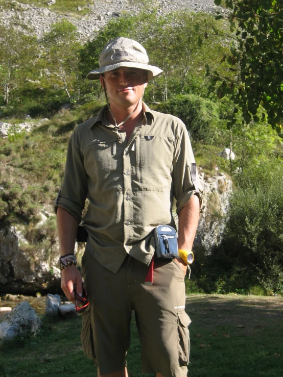 a man in a hat standing next to some rocks and a hill