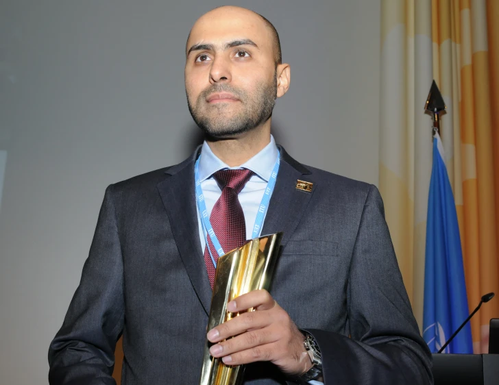 man wearing suit holding an award medal during a ceremony