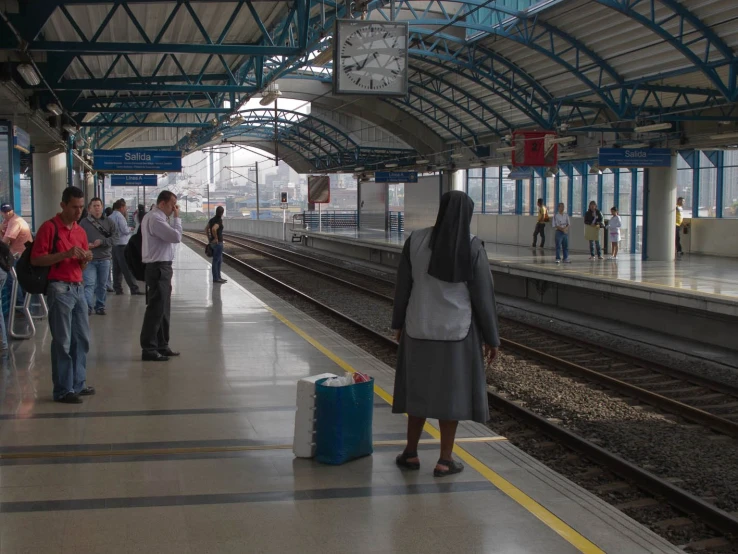 people are waiting on train tracks in a station