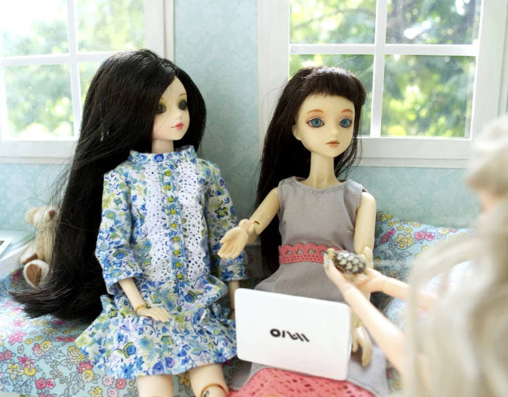 two doll dolls are sitting on a bed while one holds a laptop and another holds a small stuffed animal
