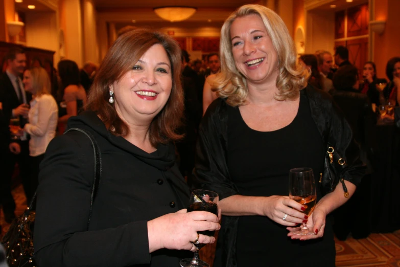 a pair of women pose for the camera holding wine glasses