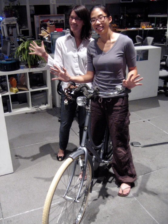 two women are posing with a bicycle on display