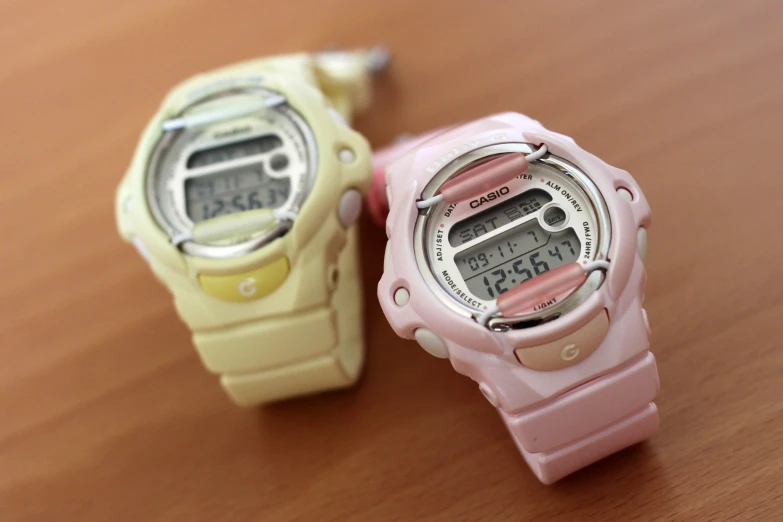 two watches that are both pink and yellow on a table