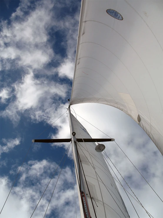 an upward view of a white sail boat with the sails down