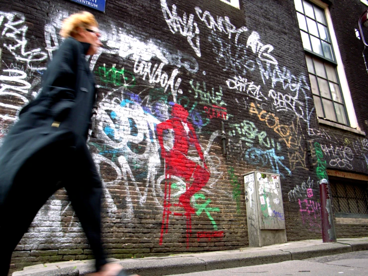 a woman walking down the sidewalk in front of a building covered in graffiti